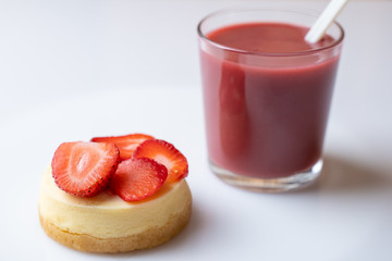 A slice of strawberry cheesecake with a nice raspberry drink in a glass on a white table
