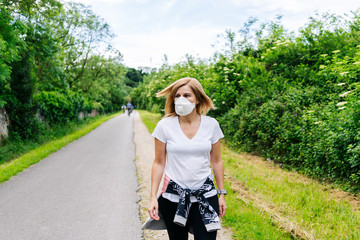A woman with face mask walking through a park in the city