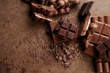 Composition of bars and pieces of different milk and dark chocolate, grated cocoa on a brown background top view close up