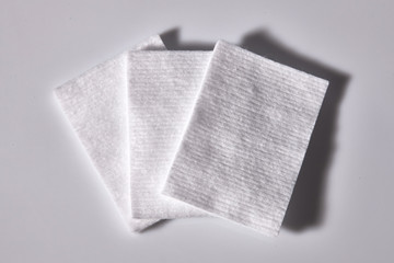 Three square cotton pads with white background.