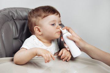 Mother using ergonomic nozzle of isotonic sea water spray for baby boy sitting on the high chair. Baby health care.