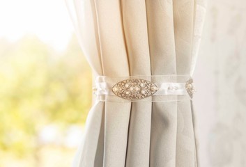 Close up view of curtain holder indoors, home decor. Minimalist gray curtain in white bedroom with sun lens flare.