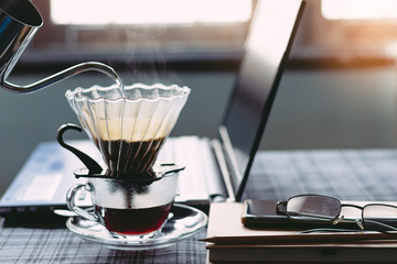 Close Up drip coffee maker with hot smoke in stainless pot, Morning coffee time with notebook computer and work equipment, Normal practice by working at home during covid-19 outbreak around the world.