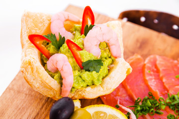 Fish platter on a wooden board. Puff basket with guacamole sauce and shrimp, lemon, olives and red fish