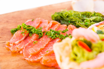 Fish platter on a wooden board. Lightly salted salmon, chuka salad and green onion decor