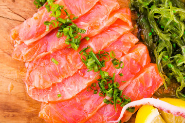 Fish platter on a wooden board. Lightly salted salmon, chuka salad and green onion decor