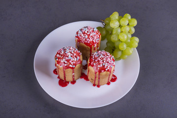 three cupcakes with red icing on a white dish with a branch of green grapes