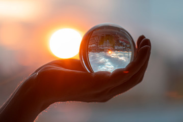 Sun and glass ball in hand, man holding crystal ball, crystal lens with sun rays and city as reflection