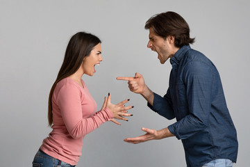 Millennial couple quarreling, shouting and blaming each other over light background