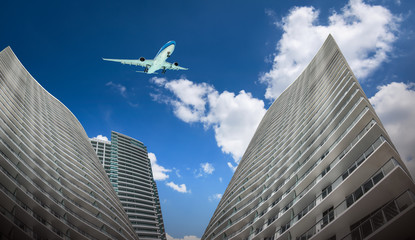 Obraz premium Commercial airplane flying over tall skyscrapers in the city. Bottom view.