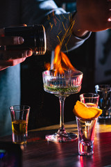 Male bartender holds fired up sugar above delicious alcohol cocktail