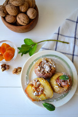 Baked apples filled with walnuts and dried apricots on a white wooden background.