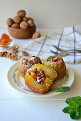 Baked apples filled with walnuts and dried apricots on a white wooden background.