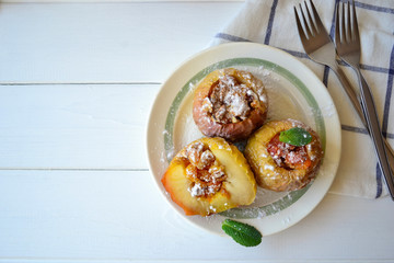 Baked apples filled with walnuts and dried apricots on a white wooden background.