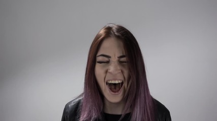 Portrait of the girl screaming loud and burying her hands in her hair feeling pain. Young woman in slow motion expresses emotion in the studio. Concept of showing different facial expressions.