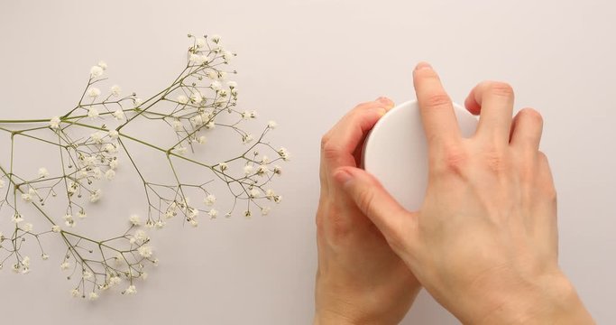 Female hands open jar of green cream or mask with flowers on white background. Luxury green mask cream to the face or body. Concept of skincare cosmetic, spa and wellness center, facial treatment