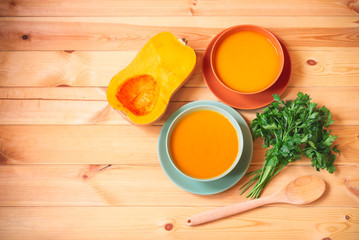 Pumpkin cream soup in bowls, half of butternut squash and fresh parsley near.