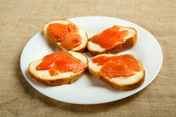 Bruschettas with sesga and cream cheese on a white plate on a linen tablecloth.