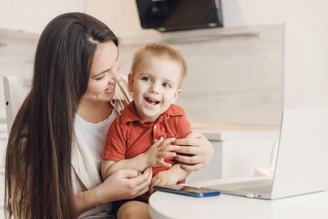 Obraz na płótnie Canvas Business mom is using online work laptop, woman spending time with her boy baby home