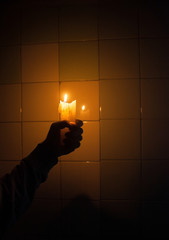 Hand holding the candle against the tiled wall