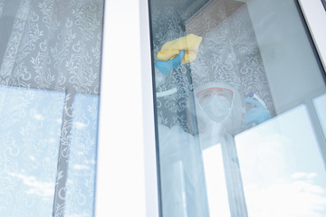 Woman wearing protective biohazard coronavirus pandemic. Cleaning service disinfects, pest control glass windows from virus