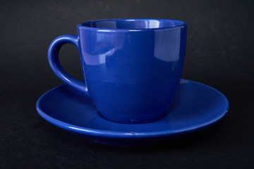 Blue cup of coffee and saucer on a black background.