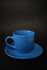 Light blue cup of coffee and saucer on a black background.