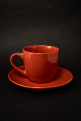 Red cup of coffee and saucer on a black background.