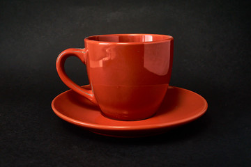 Red cup of coffee and saucer on a black background.
