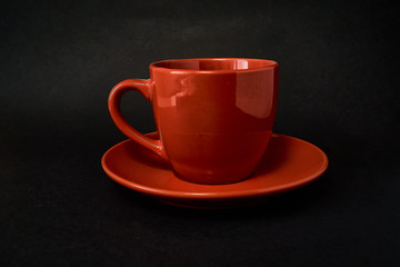 Red cup of coffee and saucer on a black background.
