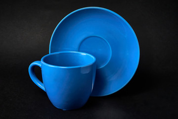 Light blue cup of coffee and saucer on a black background.