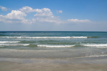 Seaside landscape with cloudy blue sky, calm sea waves and the brown, wet sand  of the beach on a summer day    