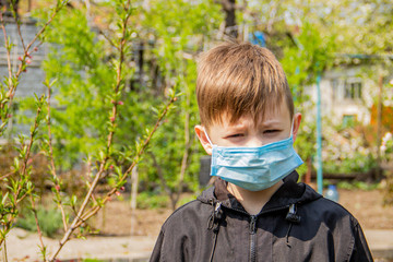 A guy in the garden dressed in a medical mask stands on a background of green trees and the sun shines on him - 345166294