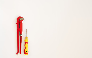 red adjustable spanner lies next to a yellow screwdriver on a white background
