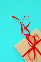 gift in beige paper with a red ribbon on a turquoise background
