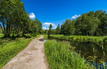 Summer landscape with a river, a path along the river, trees, grass and a blue sky with white clouds