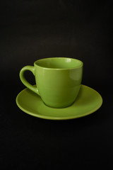Green cup of coffee and saucer on a black background.