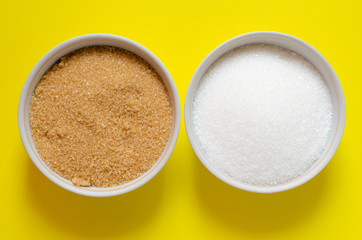 White sugar and cane-sugar in bowls on yellow background. Brown sugar.