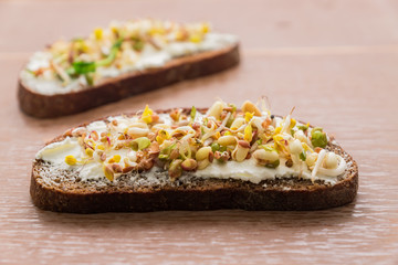 close up of rye bread sandwiches with cream cheese and sprouted mung beans, walnut, sunflower and flax on wooden background. vegan, raw food diet