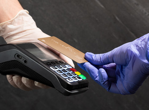 Paying with a gold card contactless at POS with medical gloves on black background.