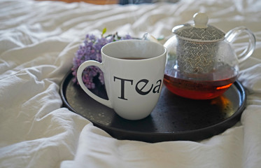 Cup of tea and teapot and lilac flower on the white tray on the bed