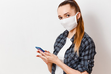 young woman in a medical mask with a smartphone in hand over a white background. Coronavirus. distance education