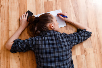 tired woman lies on the floor with a notebook and a pen