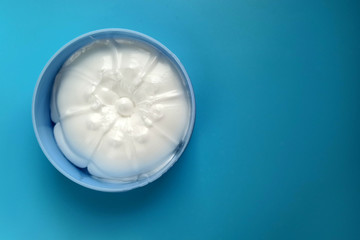 Body cream in a plastic container top view. White cream in a round box on a blue background. Cosmetics for the care of the skin of the hands, face and body.