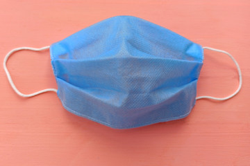 Blue medical mask with white elastic bands for the ears. Face mask on a pink background top view....