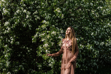 Obraz na płótnie Canvas beautiful girl in a dress basks in the sun against a background of white flowers in a flowering garden