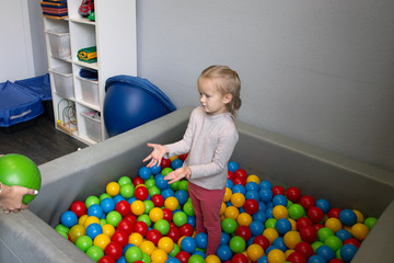little girl plays in the room of sensory integration in the pool with balls different colors - obrazy, fototapety, plakaty