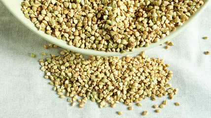 Buckwheat scattered background, raw green buckwheat in a brown clay bowl or plate. Healthy groats. Organic raw non-fried vegetarian food. The concept of a healthy and balanced diet. Diet food