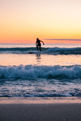 Fototapeta na wymiar Blurred surfer on longboard. small waves during beautiful sunset. surfing behind arctic circle has advantage of midnight sun. Unstad is a famous beach in Lofoten Islands