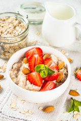 Oatmeal porridge with fresh strawberry and nuts on white background.
